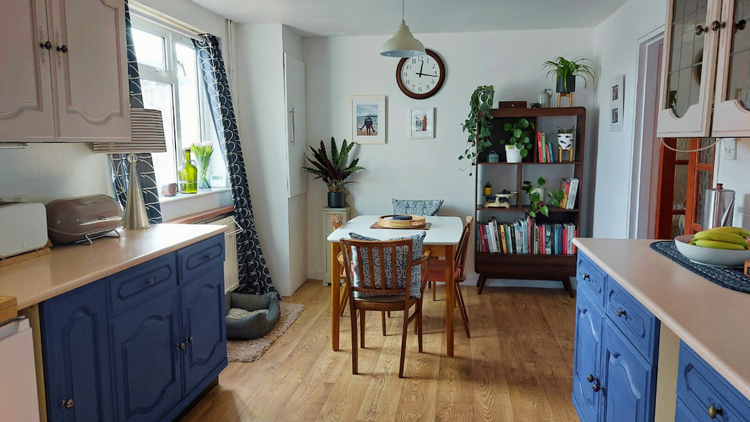 Modern kitchen featuring blue cabinets, wooden dining table, and plants, showcasing a stylish and cozy interior design.