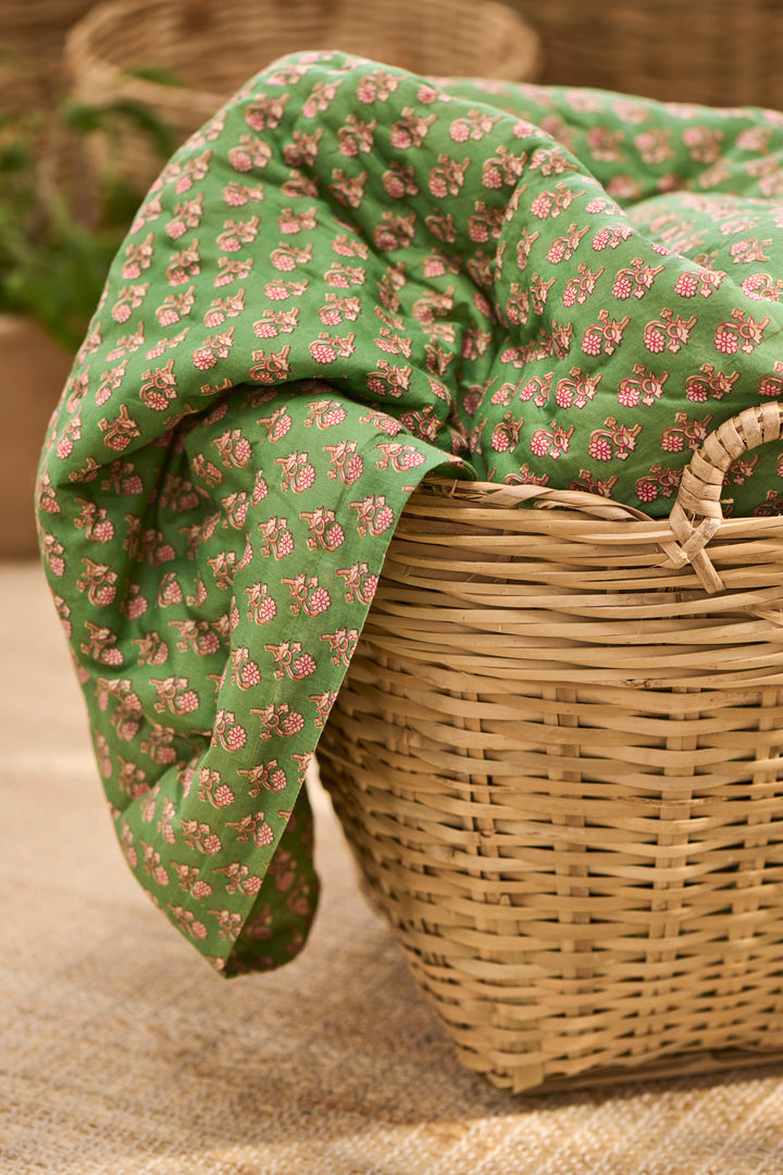 Green and pink floral quilted throw draped over a wicker basket, by Source for the Goose, Devon.