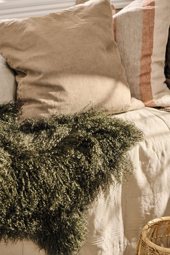 Dark green Tibetan lamb fur throw adds elegance and warmth to a beige sofa with plush pillows, perfect for cozy relaxation. Source for the Goose Devon.