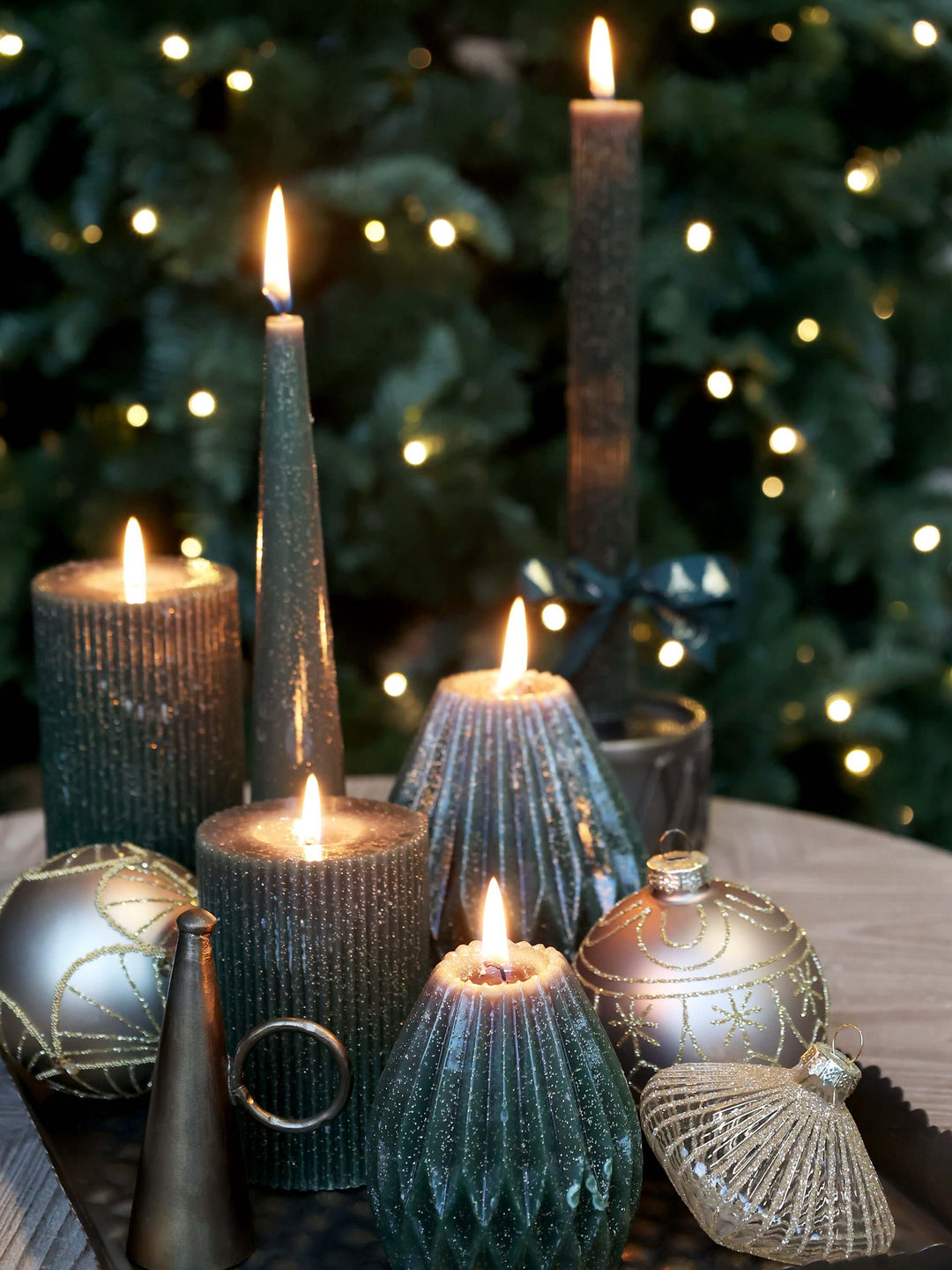 Atmospheric setting with an antique olive green pillar candle featuring grooves and a glittery finish among a variety of similar candles