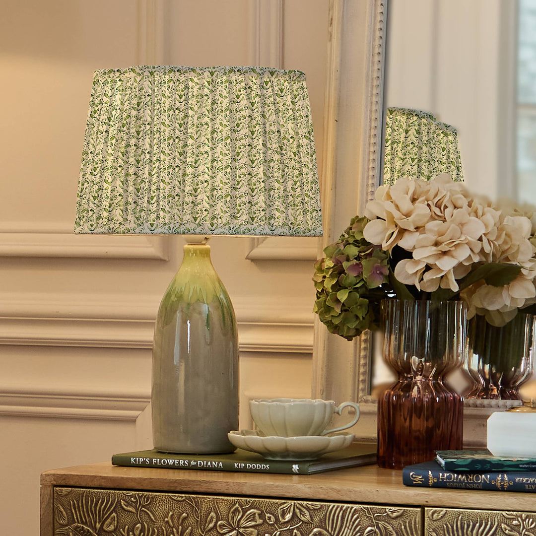 Juna pleated scalloped lamp shade in sage on a decorative table, enhancing elegant home decor with floral design.