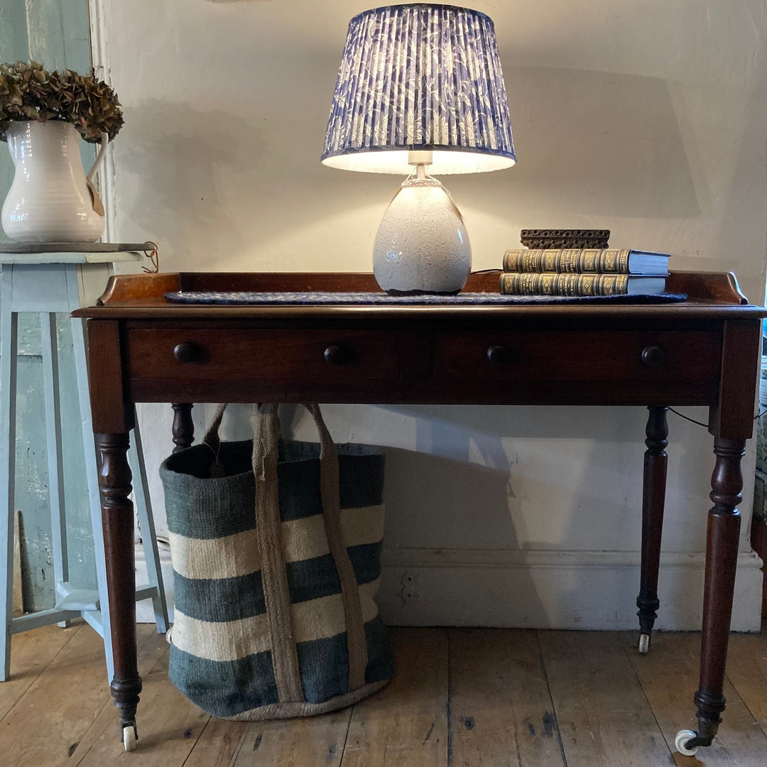 Victorian antique mahogany console table with drawers, lamp, books, and a striped bag in a cozy setting. Source for the Goose Devon.