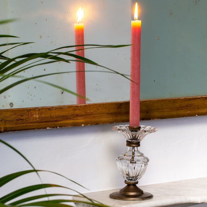 Vintage-style glass and gold candle holder with pink candle on mantelpiece, reflecting its flame in antique mirror.