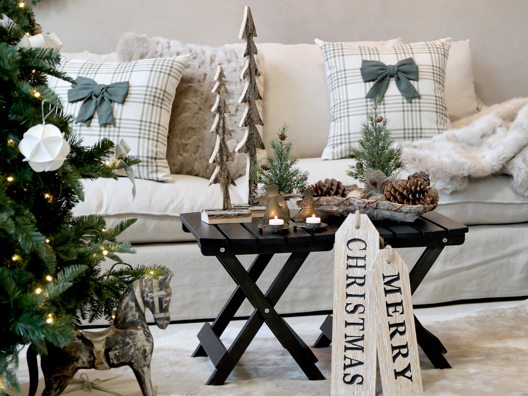 Cozy holiday living room with Christmas decorations, pine cones, tea lights, and Merry Christmas signs on a rustic table.