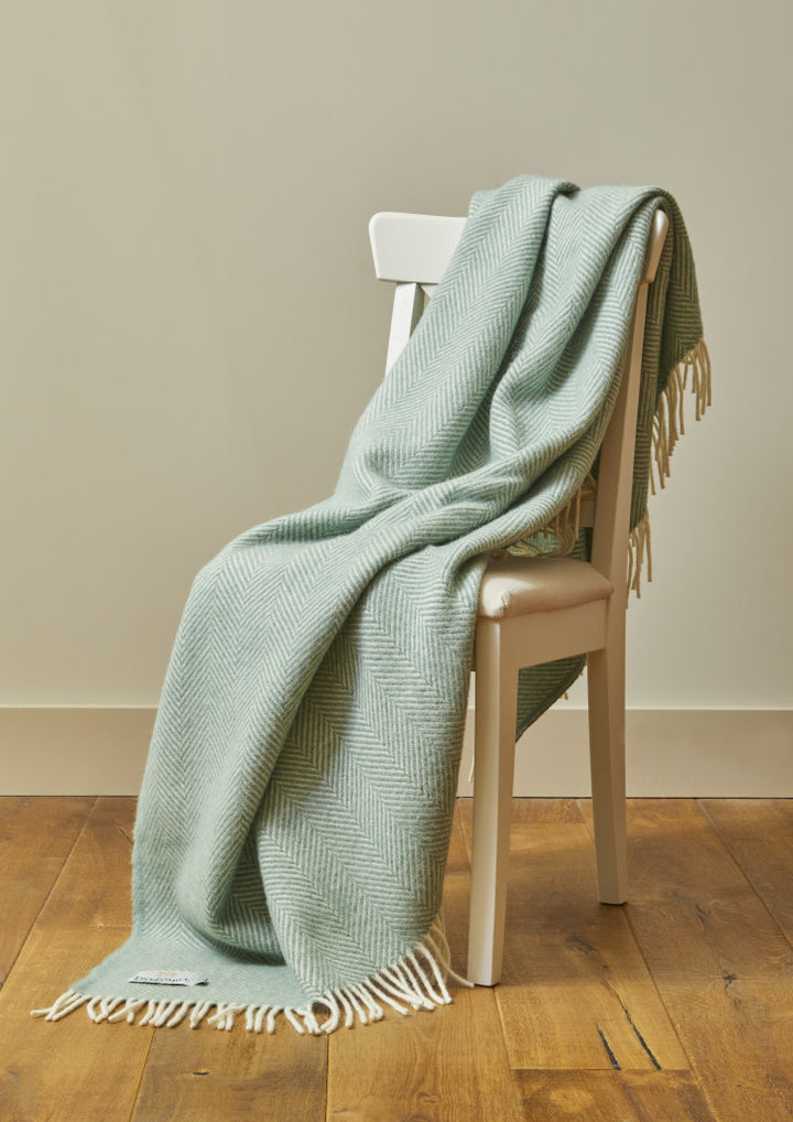 Sea green Tweedmill Fishbone blanket with cream tassels draped over a chair, sold by Source for the Goose, Devon.