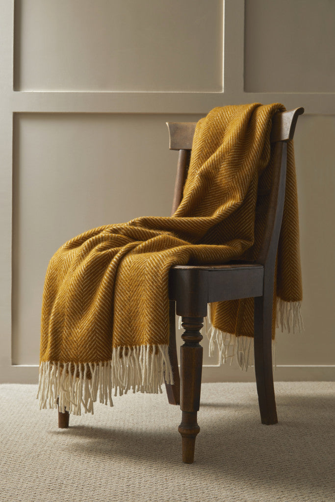 Tweedmill Fishbone English Mustard Blanket with cream tassels draped over wooden chair, available at Source for the Goose Devon.