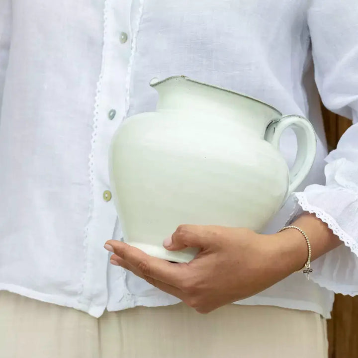 Person holding handmade short glazed white ceramic jug with a sturdy handle and spout, perfect for rustic home and vintage style decor.