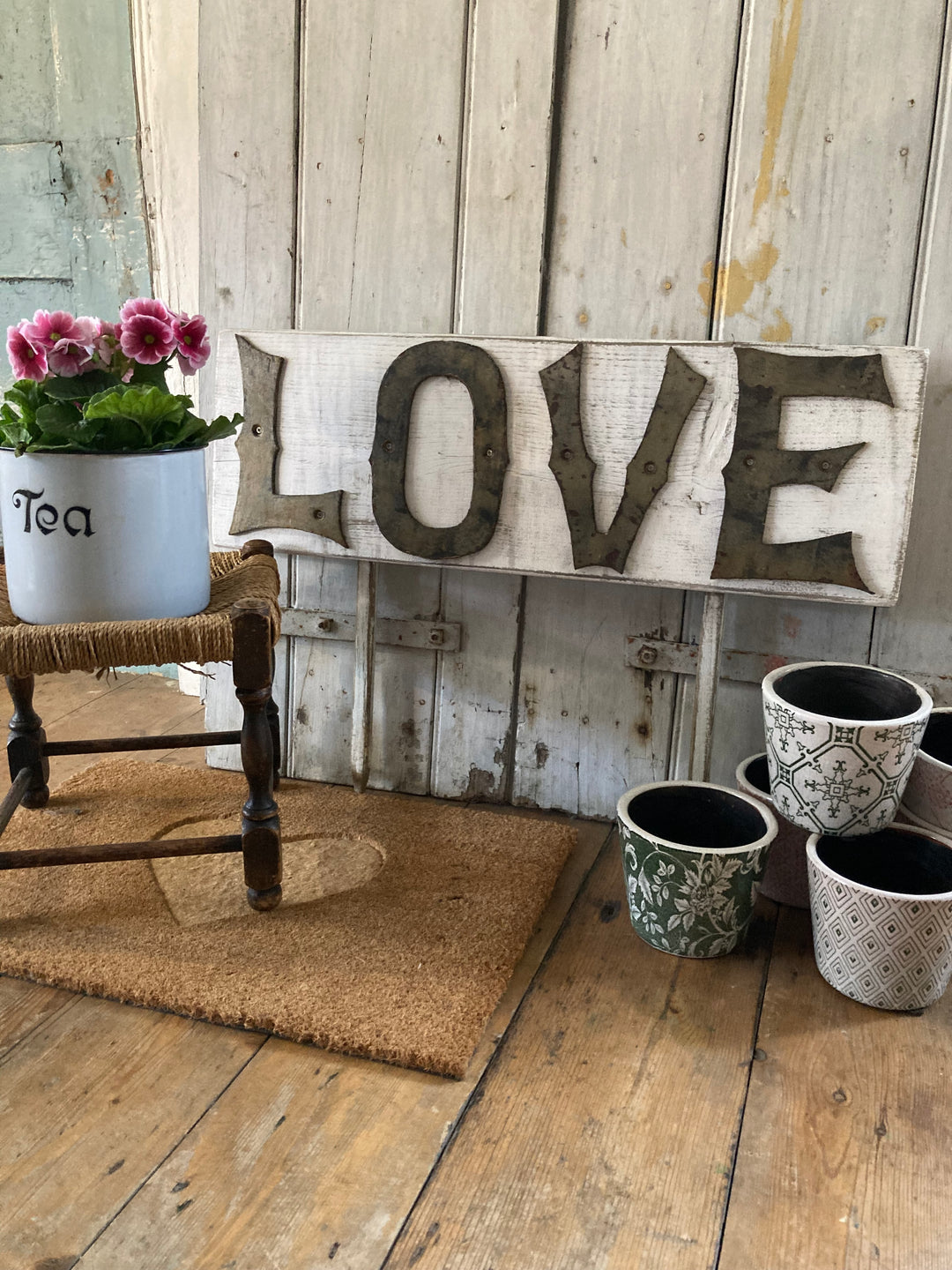 Rustic LOVE sign with vintage letters on a white wooden background, featuring a potted plant and decorative pots.