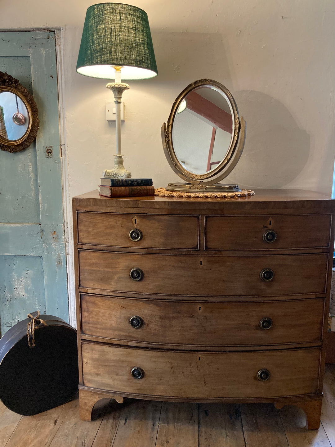 Mahogany Bow Front Chest of Drawers with brass drop handles, lamp, and mirror, sourced from Source for the Goose, Devon.