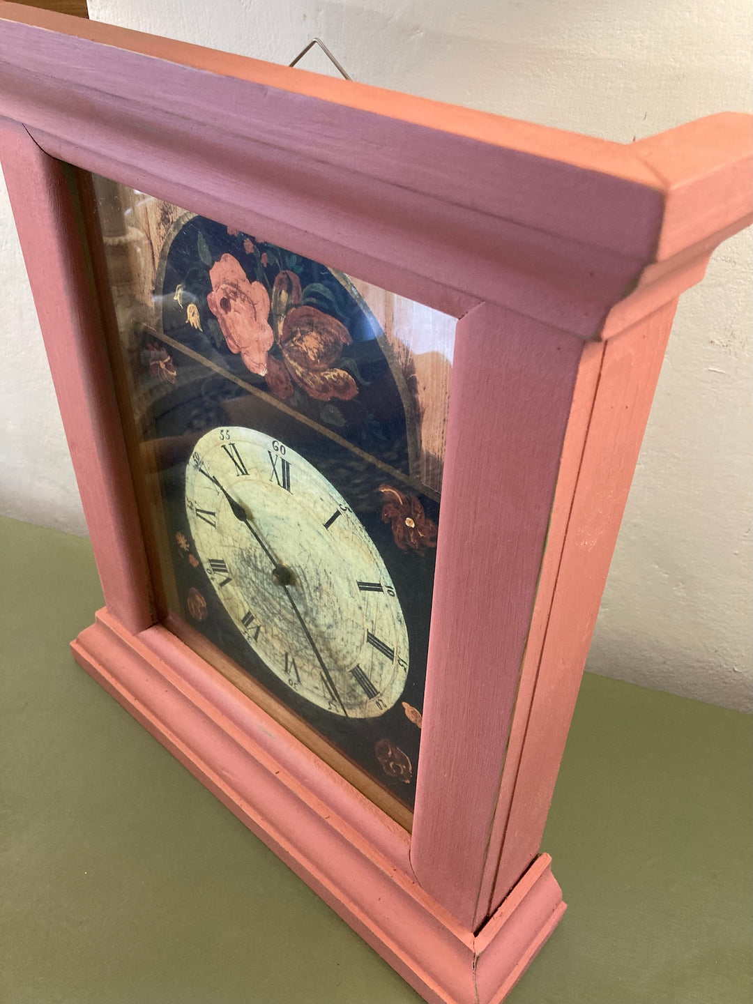 Country style painted wall clock with floral design and coral pink frame, adding vintage charm to any room. Source for the Goose, Devon.