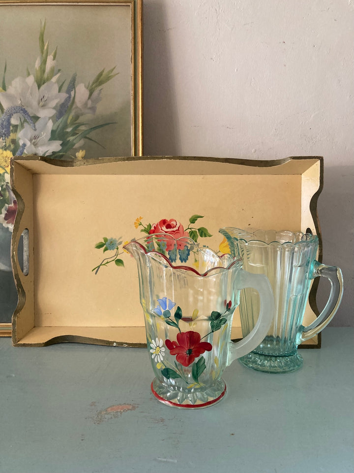 Pretty painted 1930s vintage tray with floral design beside glass pitchers, adding charm to home decor.