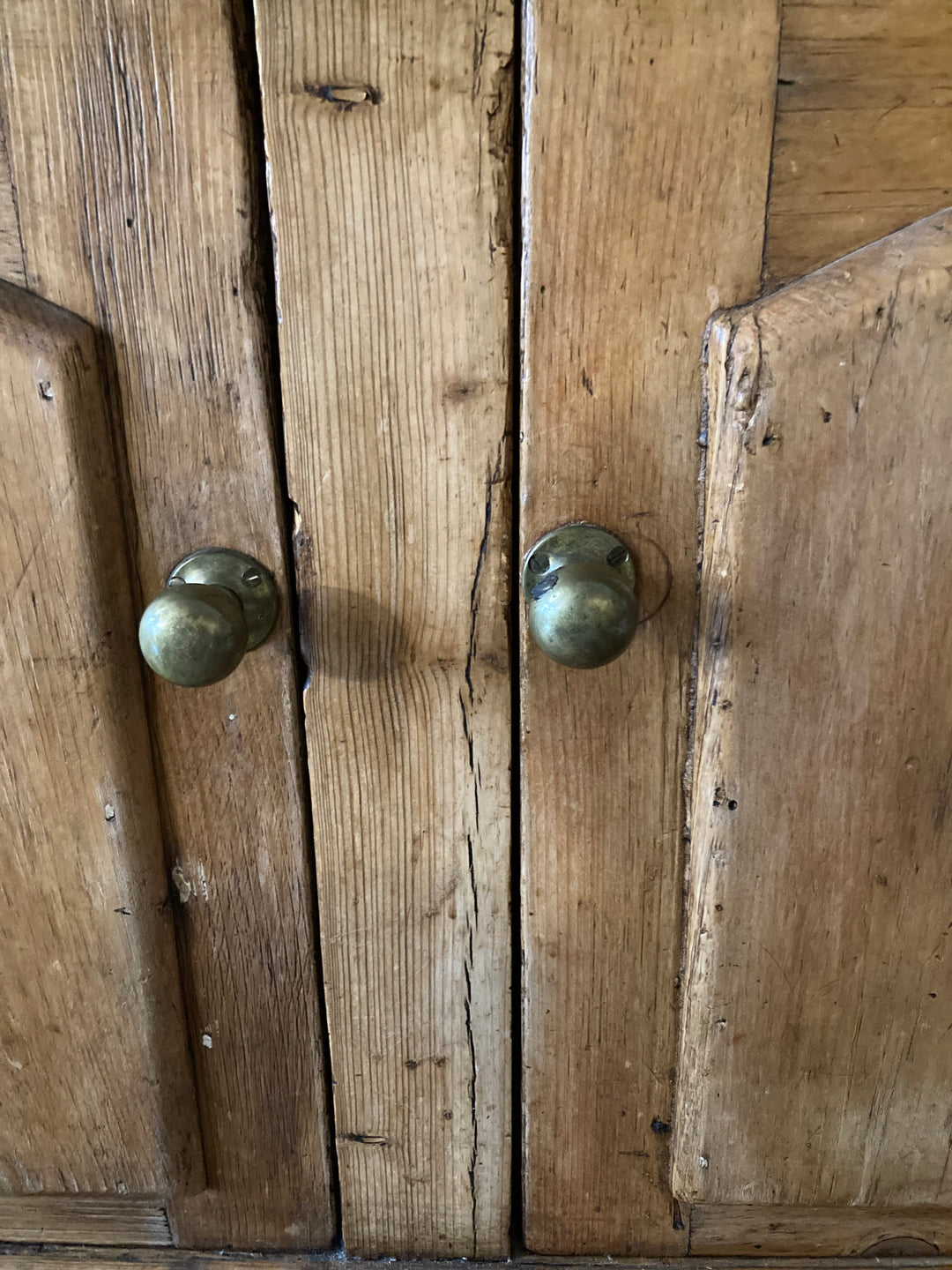 Close-up of brass handles on rustic antique pine sideboard doors, showcasing vintage charm and craftsmanship.