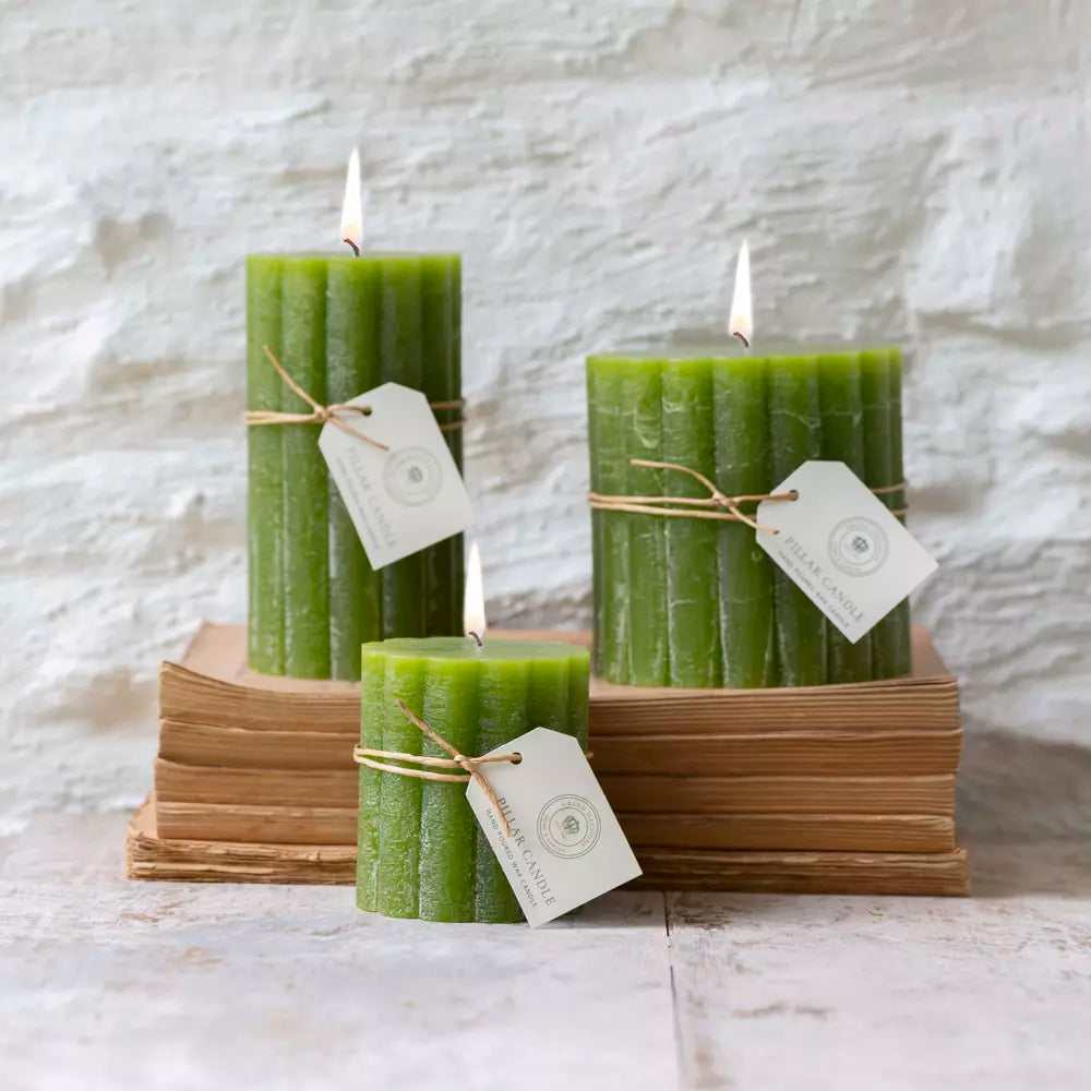 Rustic scalloped pillar candles in fern green, elegantly arranged on stacked books by Source for the Goose, Devon.