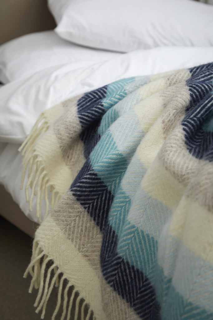 Tweedmill Seashore Blue Stripe Pure Wool Throw with herringbone design and cream fringe draped over white bed linens, Source for the Goose Devon