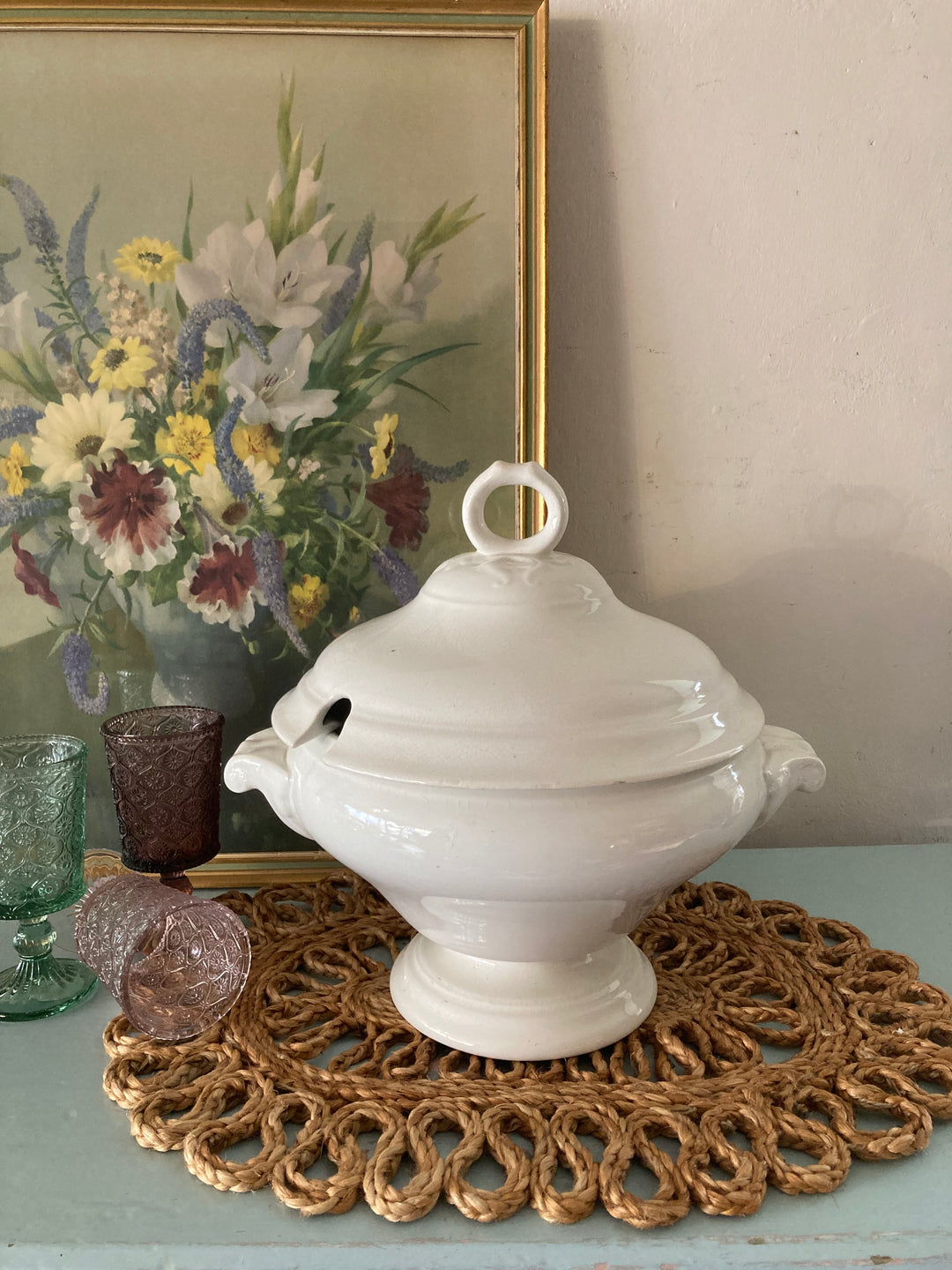 Large Antique White Tureen on a decorative table with vintage glasses and a floral painting in the background.