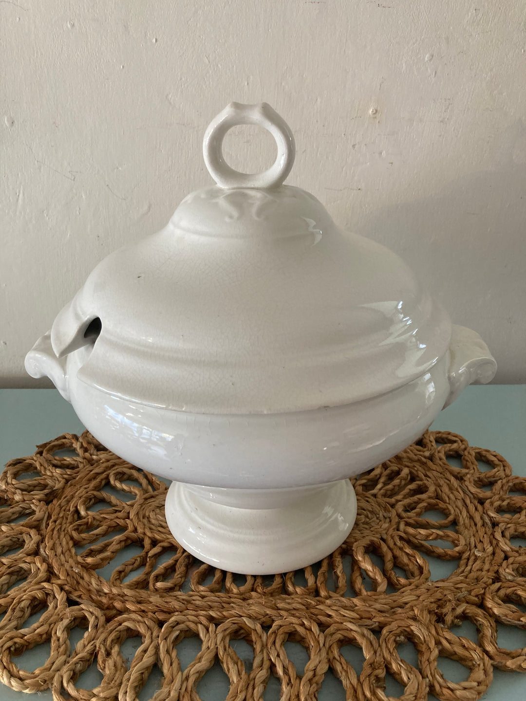 Large antique white tureen on a decorative wicker mat, perfect for rustic farmhouse decor.