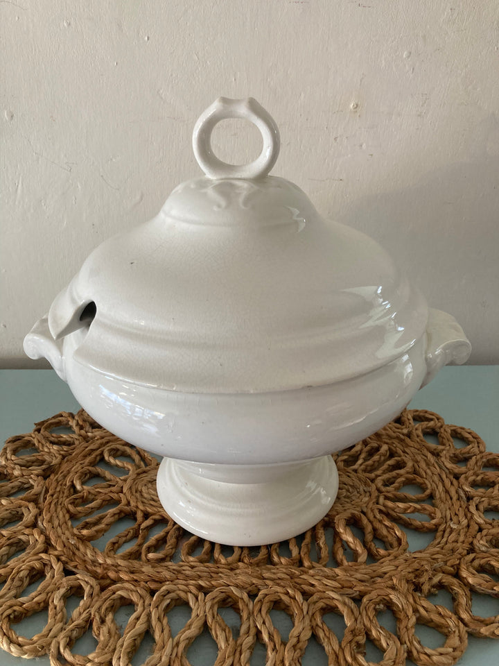 Large antique white tureen on a decorative wicker mat, perfect for rustic farmhouse decor.