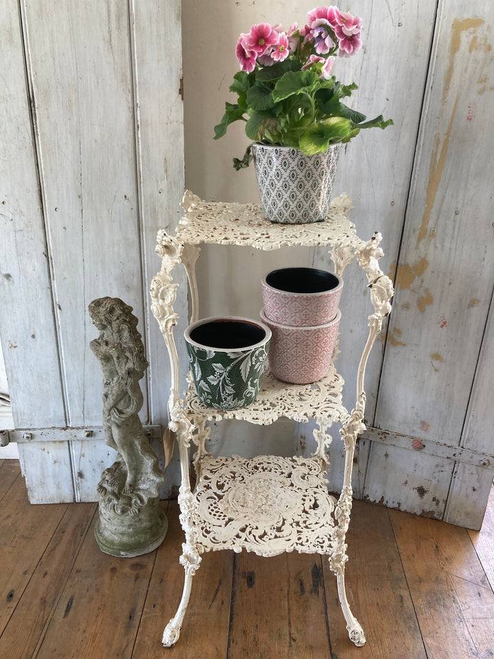 Antique White Cast Iron Plant Stand with three tiers, decorated with potted plants, adding vintage style to home decor.