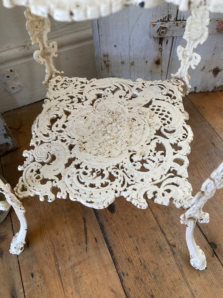 Antique white cast iron plant stand featuring intricate filigree design on the shelf, perfect for vintage home decor.