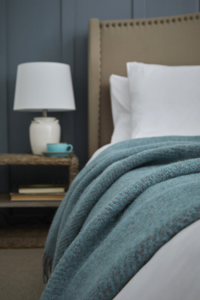 Beehive Spearmint & Grey Pure Wool Throw on bed, Source for the Goose, Devon. Blue and grey wool blanket with tassels in rustic bedroom.