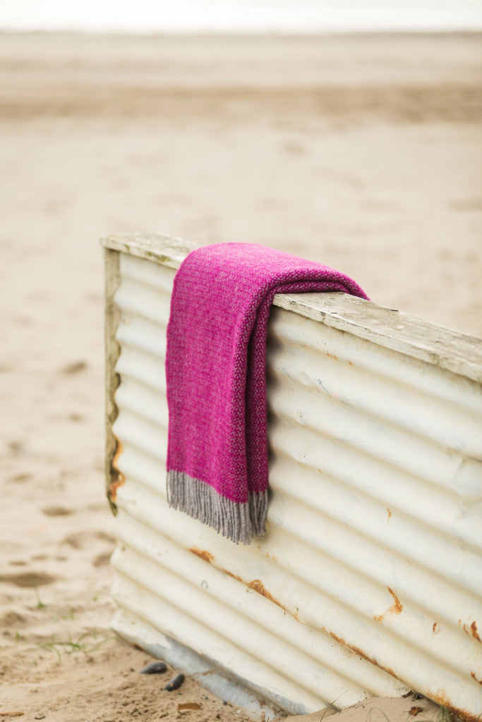 Tweedmill Lifestyle Boa Pure New Wool Blanket in Pink draped over a rustic wooden surface on a beach, available at Source for the Goose in Devon.