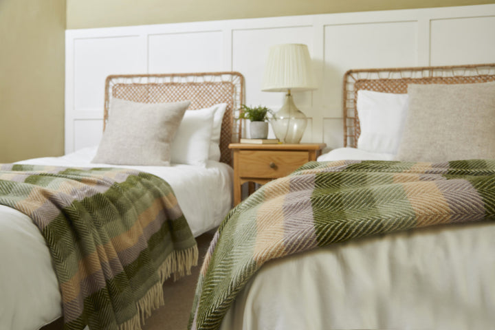 Tweedmill Botanical Green Stripe Pure Wool Throw on twin beds with cream tassels, enhancing room decor and offering luxury warmth from Source for the Goose in Devon.