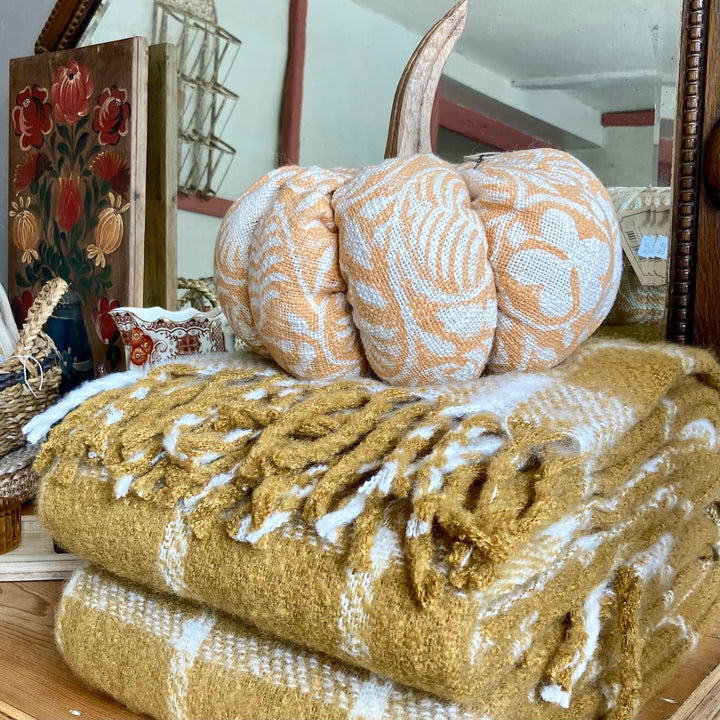 Burnt orange fabric pumpkin with wooden stem on woolen blanket, displayed among vintage collectibles at Source for the Goose, Devon.