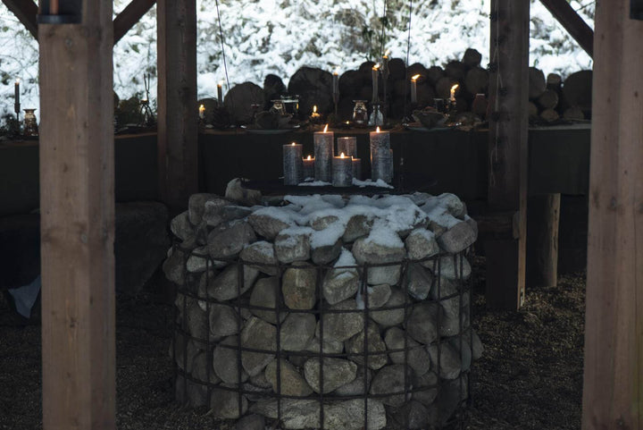 Rustic dark green candles on a stone pedestal create a cozy winter ambiance outdoors