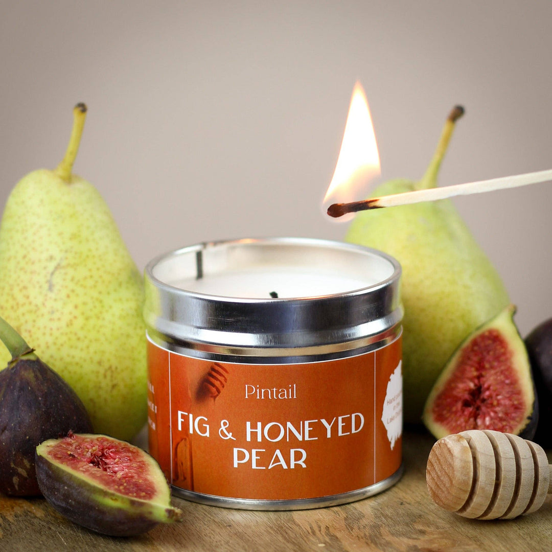 Fig & Honeyed Pear Classic Tin Candle by Pintail being lit, surrounded by fresh figs and pears, Source for the Goose Devon