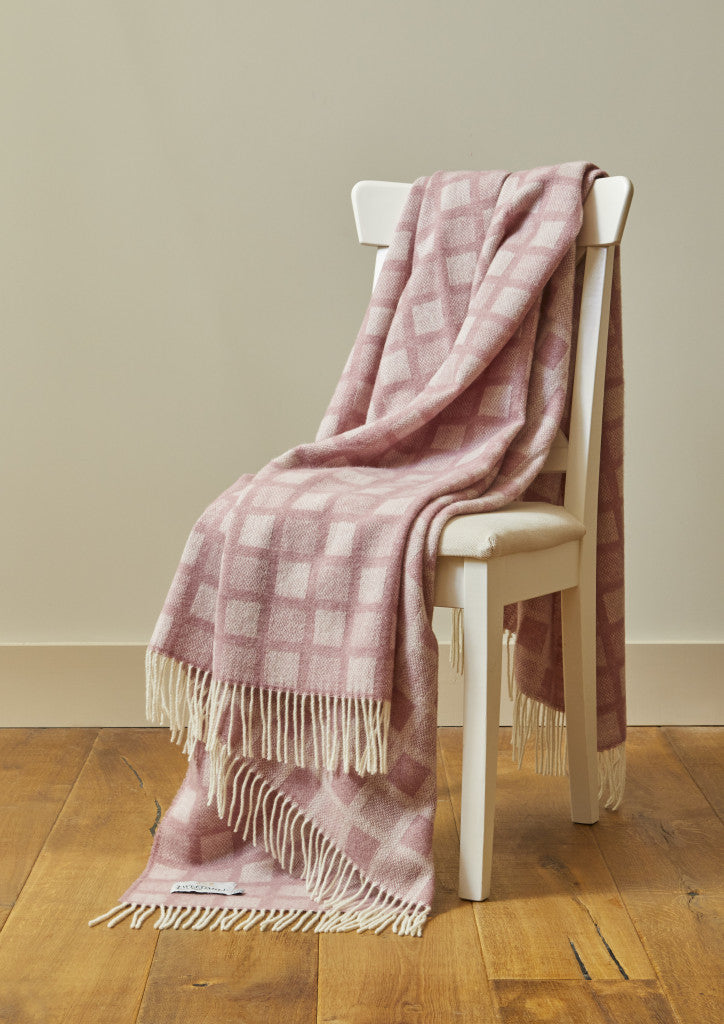 Tweedmill Sunken Pink Manhattan Wool Throw with cream tassels draped over a white chair, available at Source for the Goose in Devon.