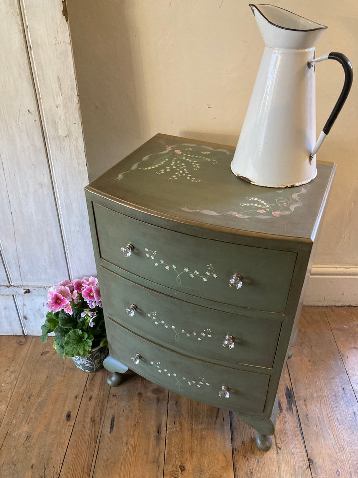 Small chest of drawers with hand-painted flowers, green finish, topped with a vintage pitcher and flower pot.