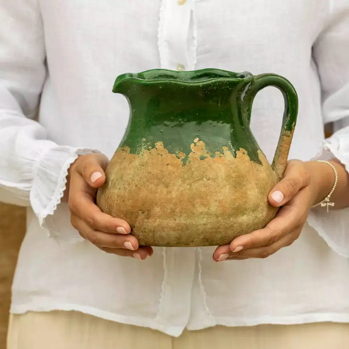 Rustic green terracotta jug with vintage charm, held by person in white blouse, featuring rich green glaze and earthy base, perfect as decor or pitcher.