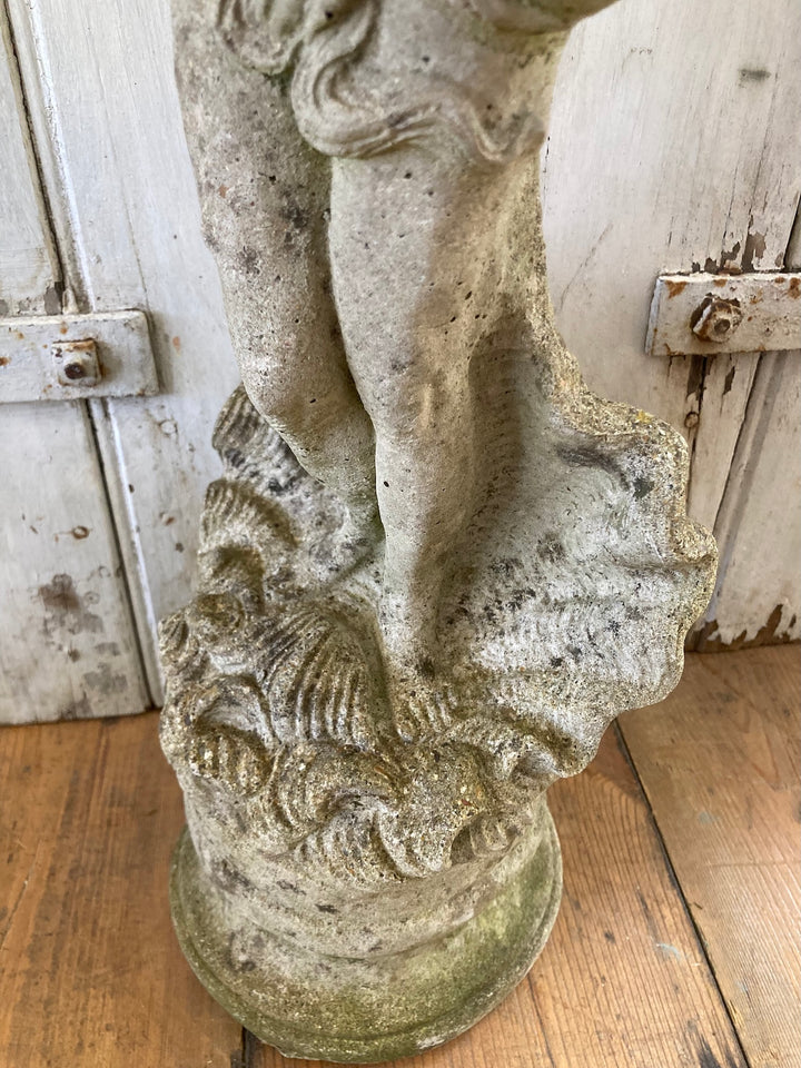 Close-up of a stone garden statue of a lady with detailed base in a shell, showcasing aged patina and elegant design from Source for the Goose.