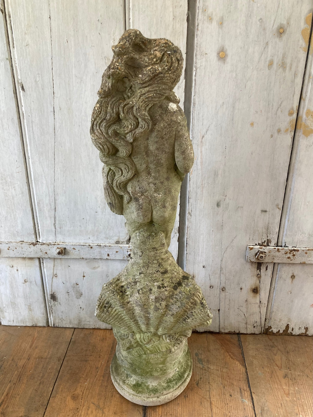 Aged stone garden statue of a lady with long hair, elegantly posed on a shell, ideal for outdoor decor from Source for the Goose Devon.