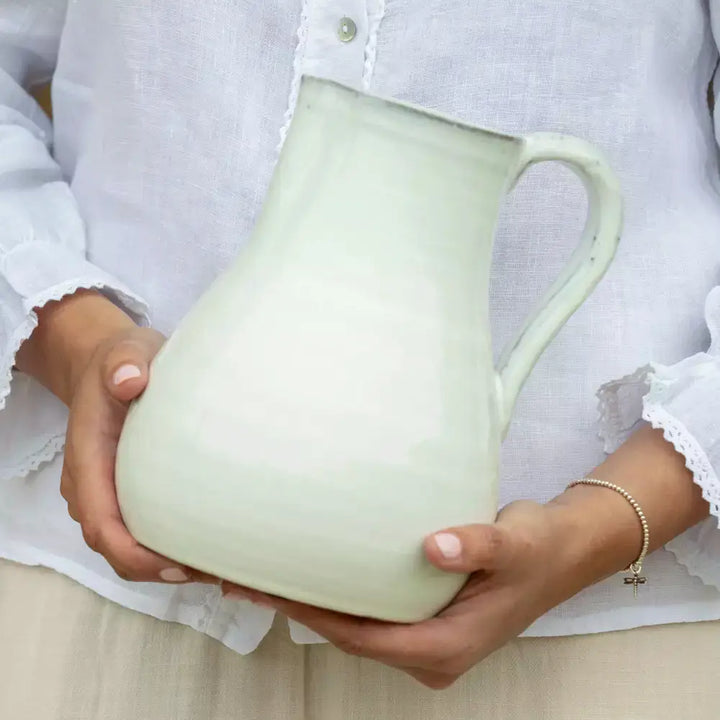 Person holding a vintage style glazed white jug, perfect for rustic home decor or serving beverages.