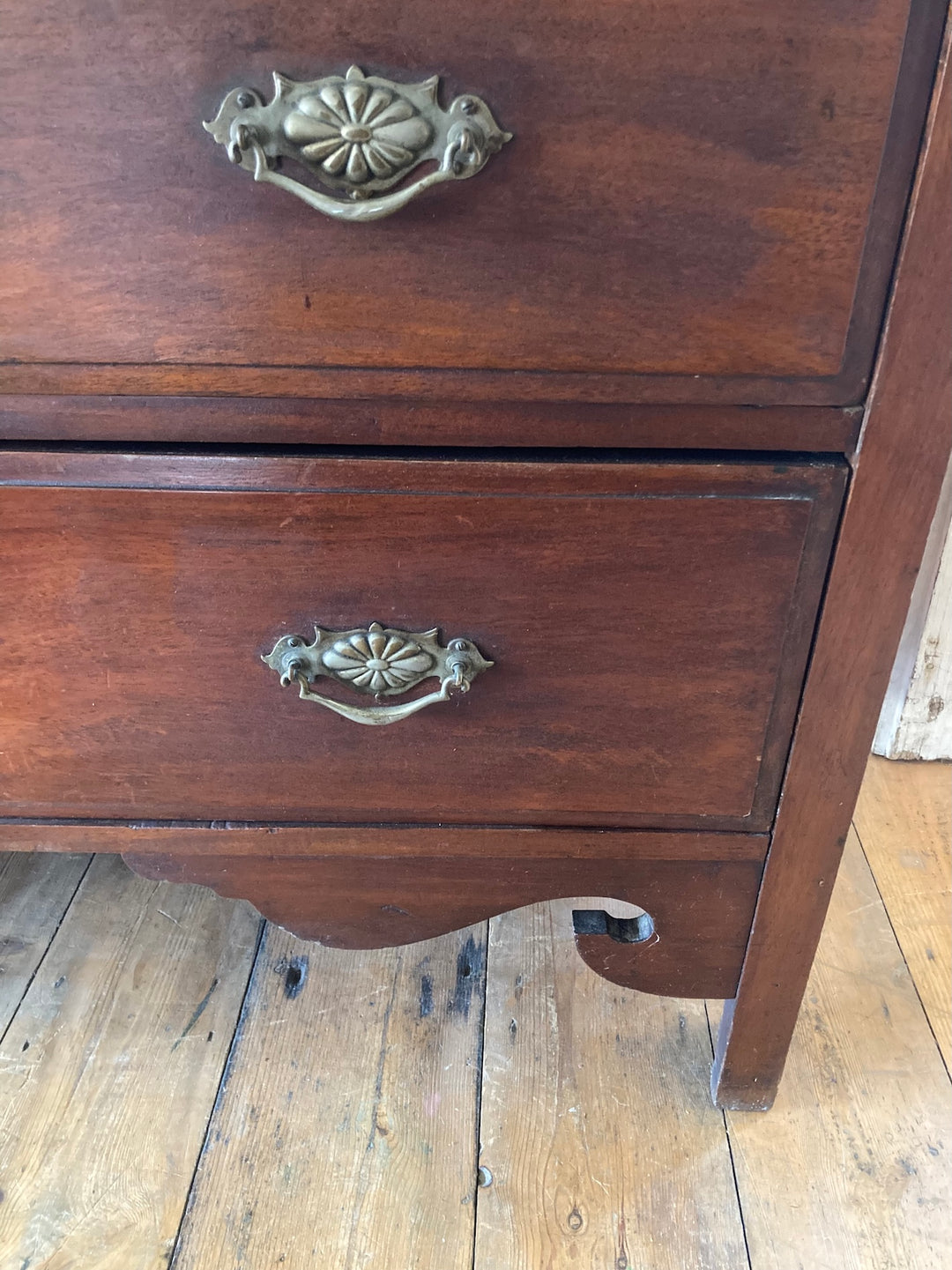 Close-up of tall two over three Edwardian chest of drawers showcasing brass drop handles and antique wood finish.