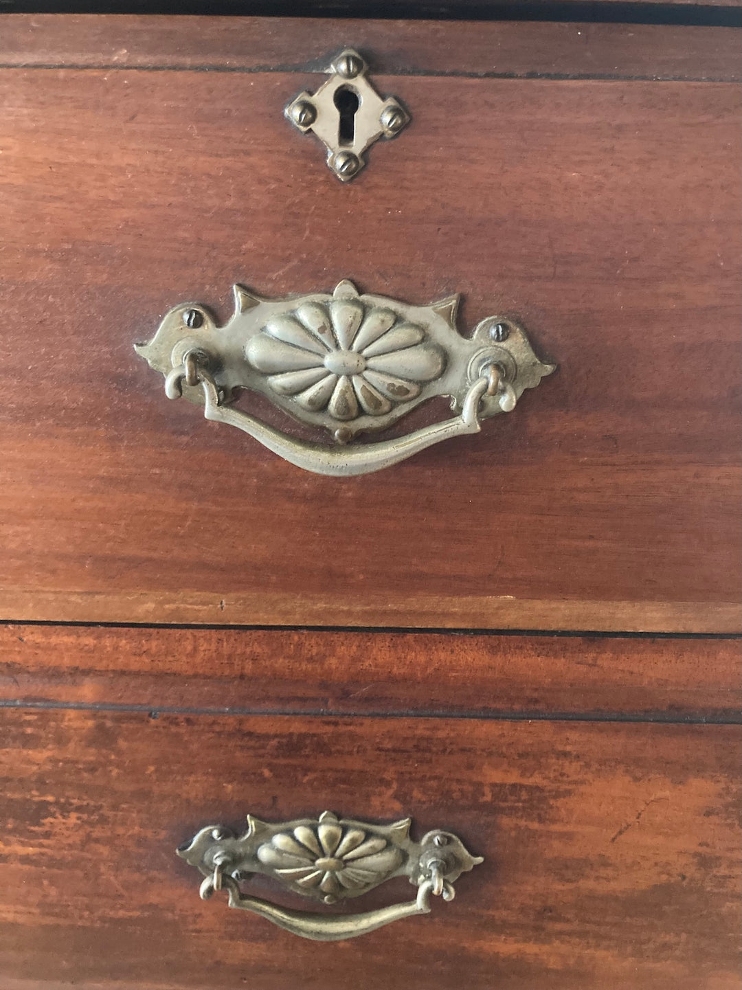 Close-up of ornate brass drop handles on an antique wooden chest of drawers, emphasizing Edwardian craftsmanship.