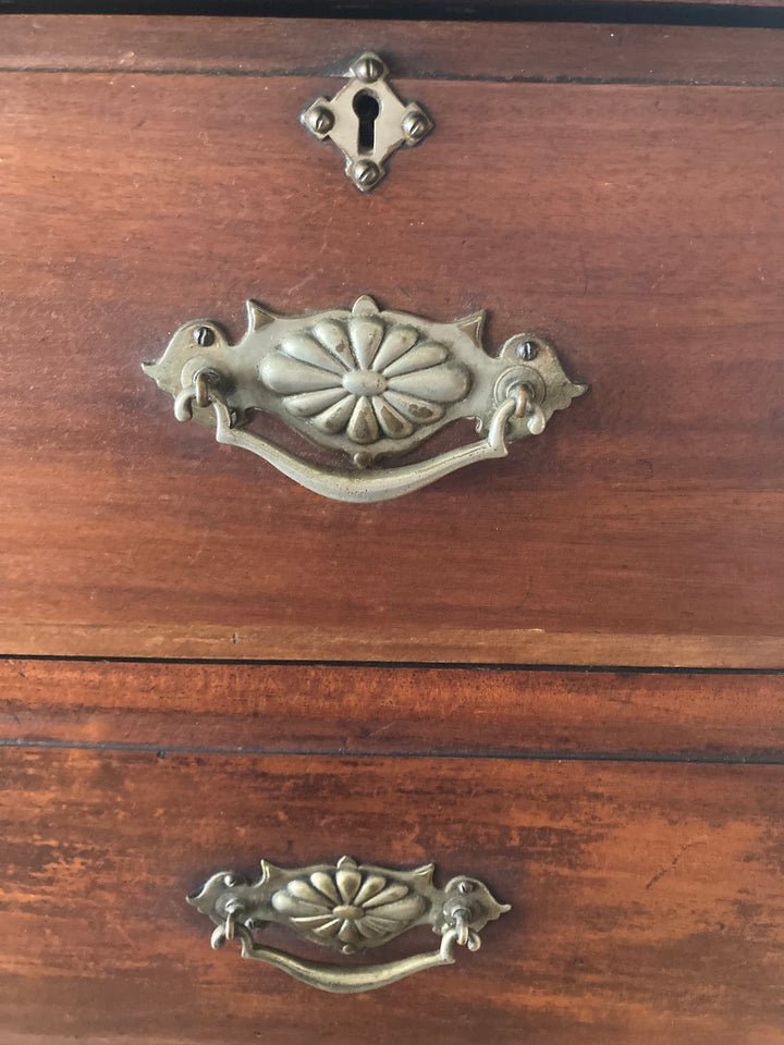 Close-up of ornate brass drop handles on an antique wooden chest of drawers, emphasizing Edwardian craftsmanship.