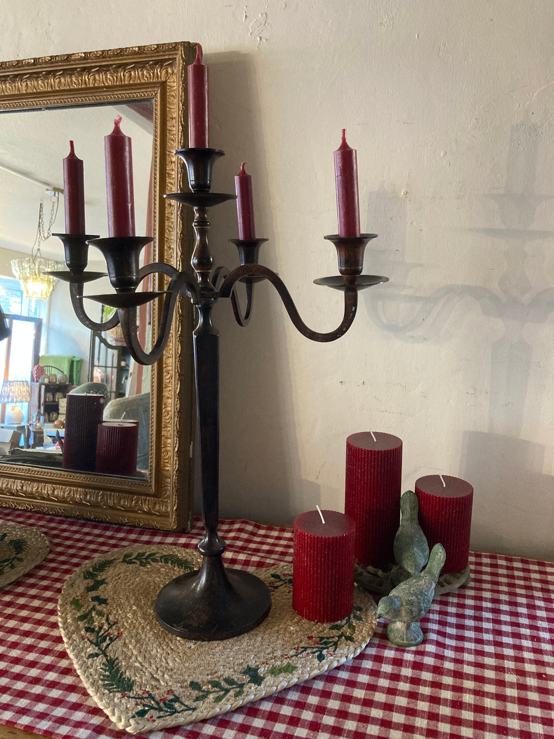 Tall vintage metal five arm candelabra with burgundy candles on a checked tablecloth, reflecting elegance and charm.