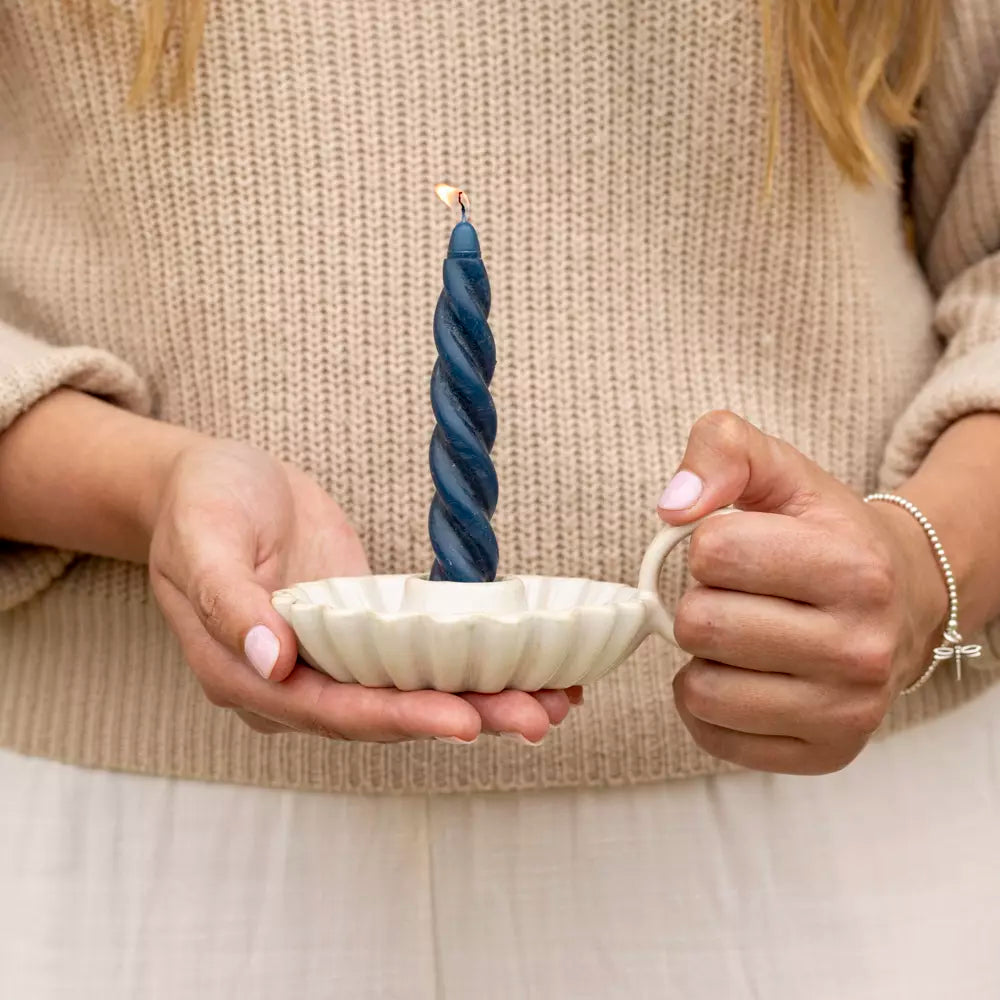 Woman holding a twisted inky blue dinner candle in a cream holder, showcasing elegant home decor for a cozy atmosphere.