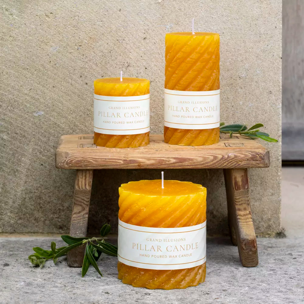 Elegant twisted warm ochre pillar candles on a wooden stool, showcasing luxury by Source for the Goose, Devon.