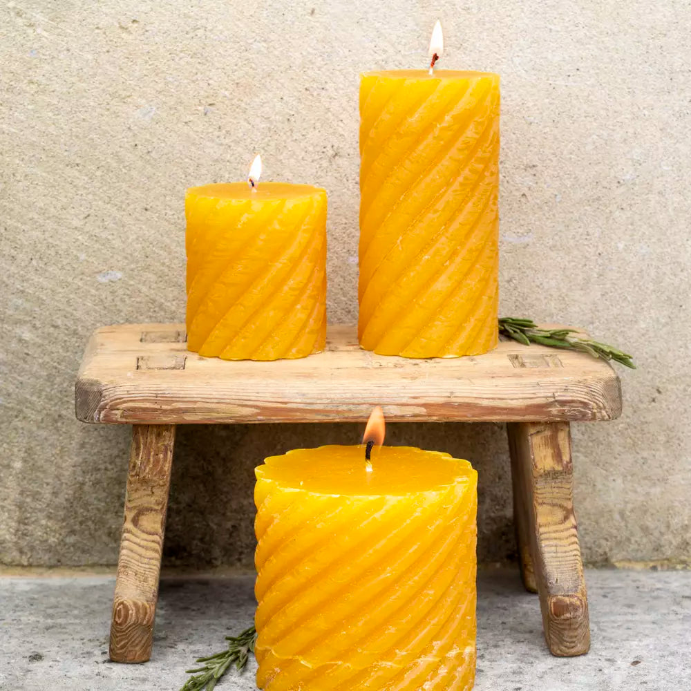 Twisted Warm Ochre Pillar Candles glowing on a wooden stand, showcasing their elegant design and rich yellow hue from Source for the Goose Devon.