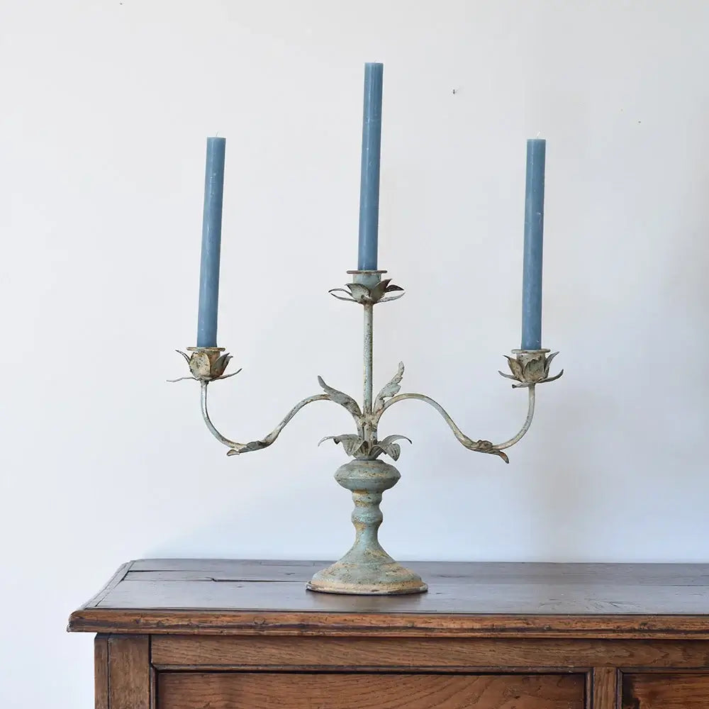 Vintage style metal candelabra with three blue candles on a wooden table, adding an elegant touch to home decor.