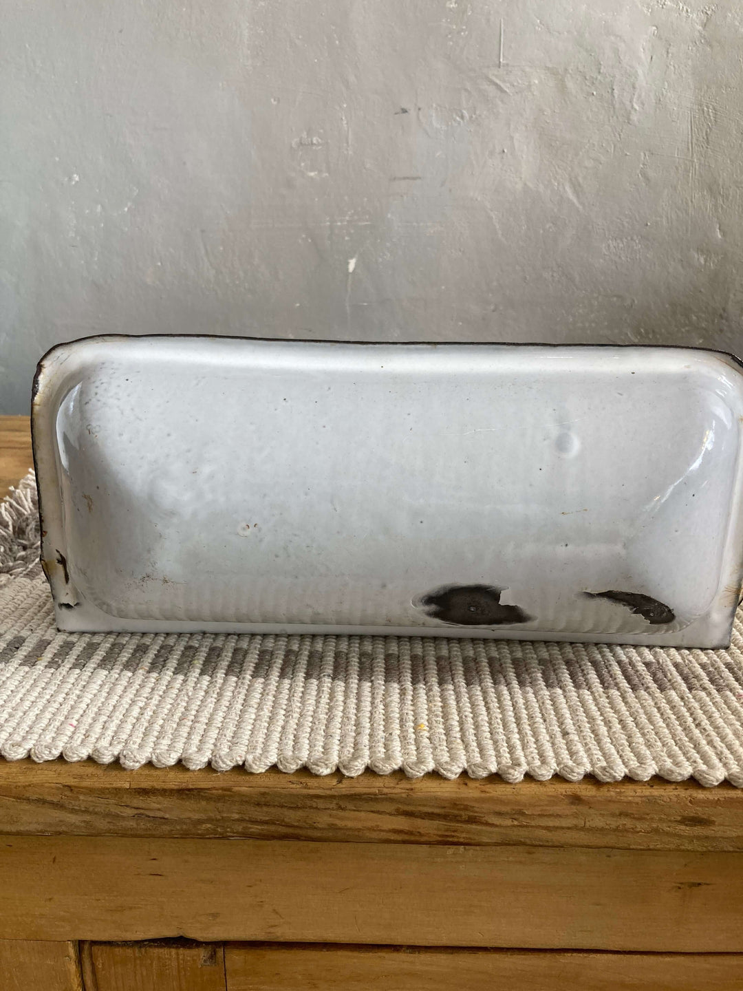 Back view of Vintage French Enamel Spoon Rest with white background and distressed details displaying rustic charm on a wooden counter.