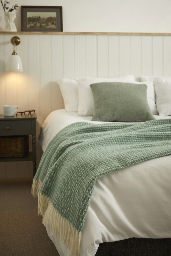 Tweedmill Waffle Sea Green Pure Wool Throw with cream tassels on a bed in a cozy room, available from Source for the Goose Devon.