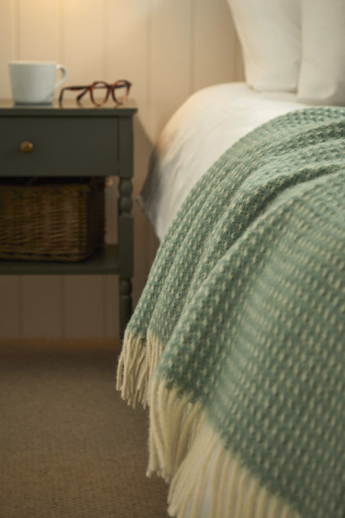 Tweedmill Waffle Sea Green Pure Wool Throw on bed with cream tassels by nightstand, available from Source for the Goose Devon