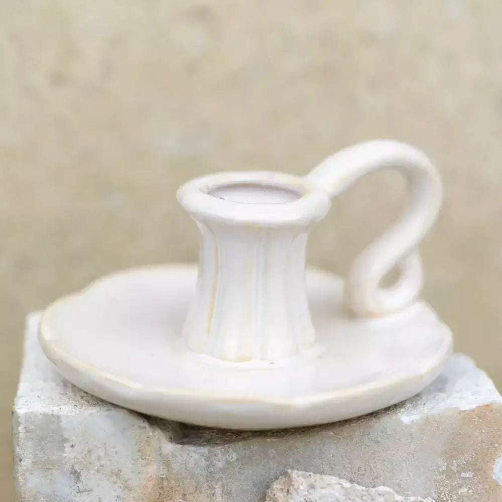 Vintage white ceramic candle holder with a handle on a rustic stone surface