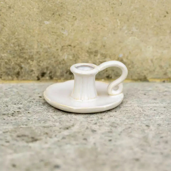 Vintage style white ceramic candle holder with handle on a concrete surface