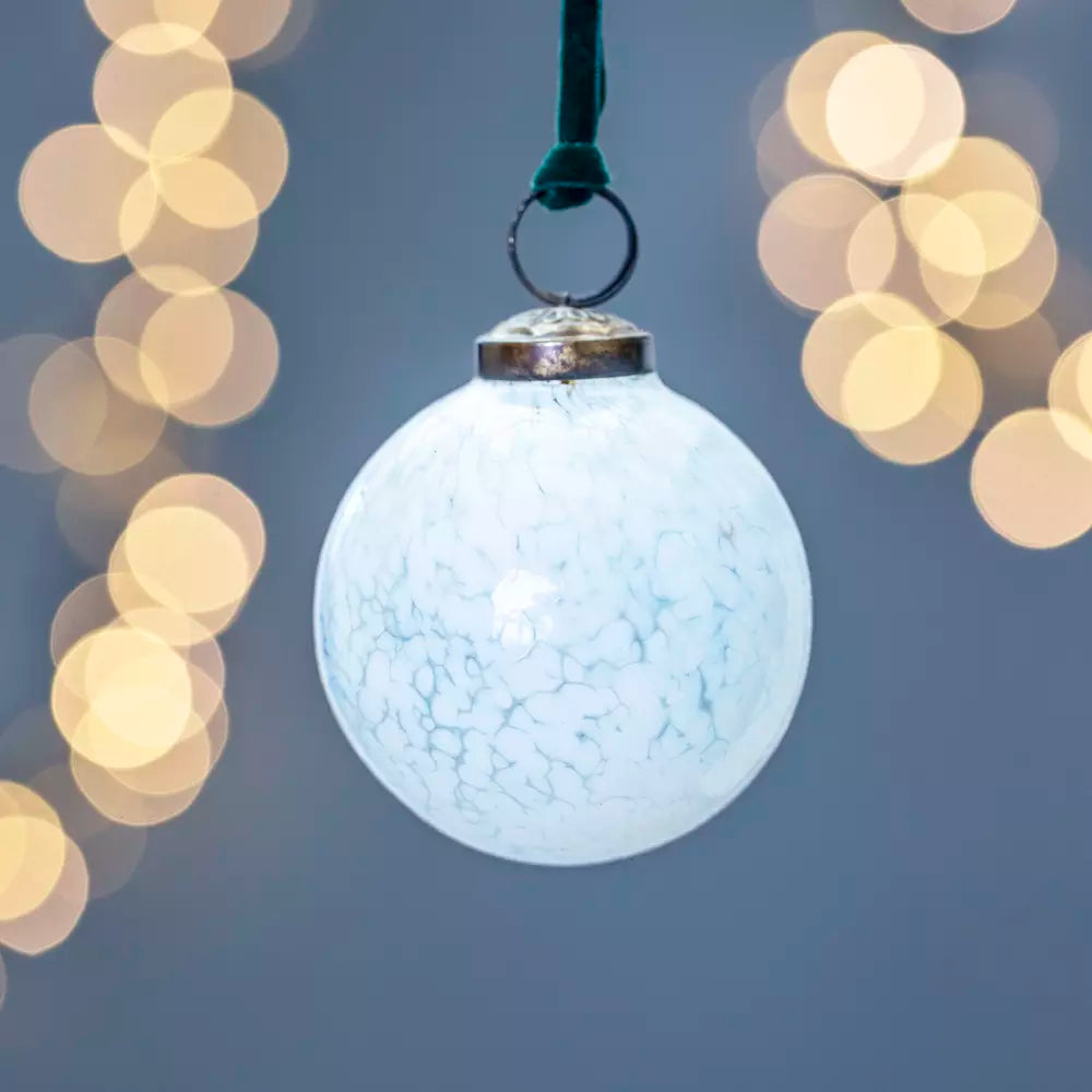 White glass Christmas decoration with teal velvet loop from Source for the Goose Devon, elegant vintage-style bauble with bokeh lights in background